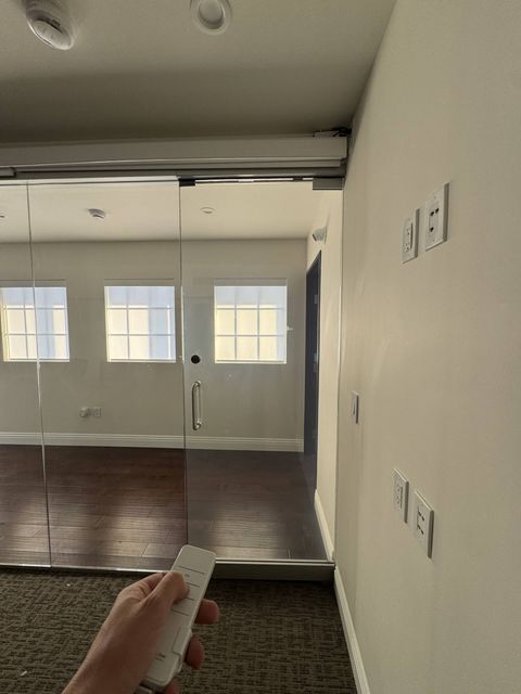 Top-hung sliding glass partition at a Hermosa Beach office in clear mode, the room beyond fully visible, with a Smart View remote in hand