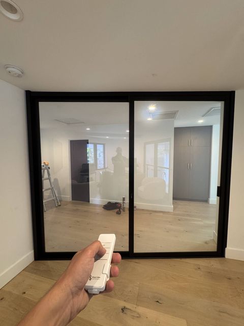 Sliding smart glass partition at a Huntington Beach home office powered clear, the room behind fully visible, Smart View remote in hand