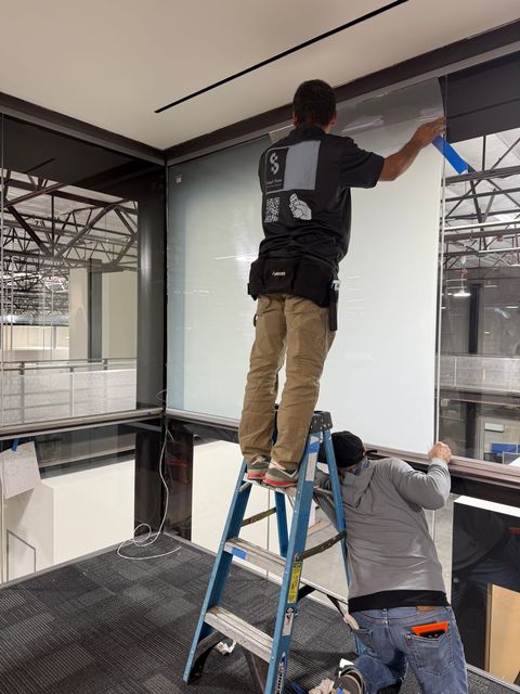 Smart View installers on ladders applying PDLC smart film to a glass-walled office mezzanine in Los Angeles