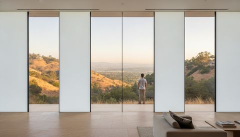 Anaheim Hills hillside great room with a wall of switchable smart glass panels — half the panels clear over a golden inland canyon and valley view, half switched to flat, evenly frosted milky-white privacy