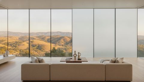 Calabasas hillside estate living room with a floor-to-ceiling switchable smart glass wall — clear panels framing the oak-studded Santa Monica Mountains, two panels switched to flat, evenly frosted milky-white privacy mode
