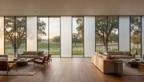Hidden Hills ranch-estate great room with a wall of switchable smart glass — half the panels crystal clear framing an oak-studded hillside and a white three-rail horse fence, half switched to flat, evenly frosted milky-white privacy mode