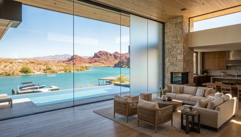 Lake Havasu City waterfront desert home with a floor-to-ceiling clear switchable smart glass wall overlooking the lake and red mountains — several glass panels switched to frosted privacy mode