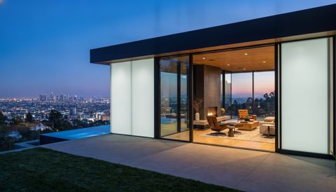 Modern Los Angeles Hills home with floor-to-ceiling clear switchable smart glass framing the LA basin and downtown skyline at dusk — several glass panels switched to frosted privacy mode