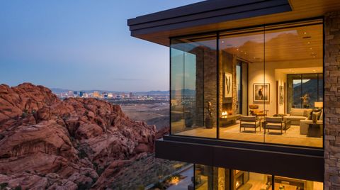 Nevada desert-modern home near Las Vegas with a floor-to-ceiling clear switchable smart glass wall framing Red Rock Canyon and the distant Strip skyline at dusk