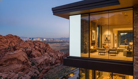 Nevada desert-modern home near Las Vegas with a floor-to-ceiling clear switchable smart glass wall framing Red Rock Canyon and the distant Strip skyline at dusk — several glass panels switched to frosted privacy mode