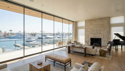 Newport Beach harbor-front home with a floor-to-ceiling clear switchable smart glass wall overlooking the marina and yachts — several glass panels switched to frosted privacy mode
