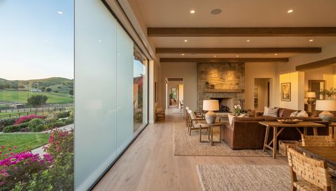 Rancho Santa Fe estate with a floor-to-ceiling clear switchable smart glass wall overlooking lush gardens and rolling hills — several glass panels switched to frosted privacy mode