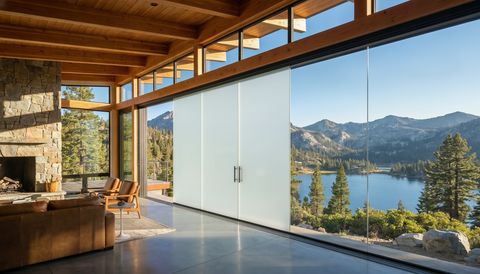 San Bernardino County mountain home with a floor-to-ceiling clear switchable smart glass wall framing the pine-covered mountains — several glass panels switched to frosted privacy mode