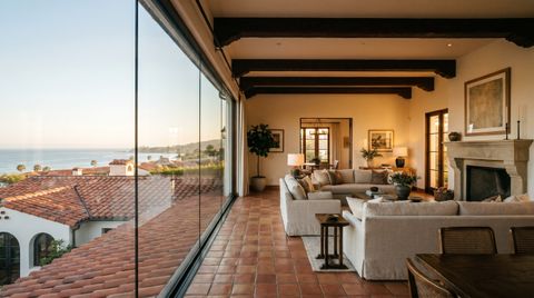 Santa Barbara Mediterranean villa with a floor-to-ceiling clear switchable smart glass wall overlooking red-tile rooftops and the ocean