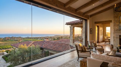 Santa Barbara County Mediterranean estate with a floor-to-ceiling clear switchable smart glass wall over red-tile rooftops and the ocean