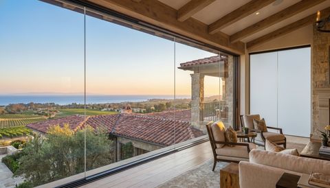 Santa Barbara County Mediterranean estate with a floor-to-ceiling clear switchable smart glass wall over red-tile rooftops and the ocean — several glass panels switched to frosted privacy mode