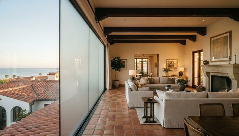 Santa Barbara Mediterranean villa with a floor-to-ceiling clear switchable smart glass wall overlooking red-tile rooftops and the ocean — several glass panels switched to frosted privacy mode