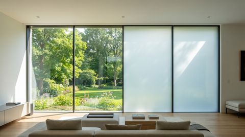 A wall of windows with switchable smart film — the left half clear showing a garden, the right half switched to frosted privacy