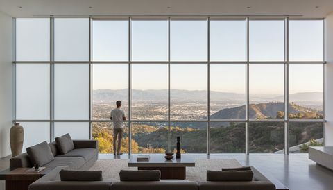 Modern Tarzana hillside living room south of Ventura Boulevard with a wall of switchable smart glass framing the San Fernando Valley below and the oak-covered Santa Monica Mountains foothills — half the panels crystal clear, half switched to flat, even, milky-white frosted privacy mode
