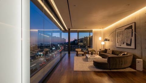 West Hollywood design-district interior with a floor-to-ceiling clear switchable smart glass wall overlooking the Sunset Strip at night — several glass panels switched to frosted privacy mode