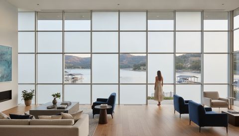 Modern Westlake Village lakefront living room with a wall of switchable smart glass framing Westlake Lake and the Conejo hills — half the panels crystal clear, half switched to flat, even, milky-white frosted privacy mode