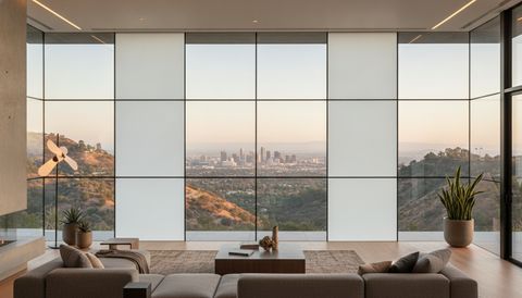 Woodland Hills hillside home with a wall of switchable smart glass above the San Fernando Valley — half the panels crystal clear framing the Warner Center skyline, half switched to flat, evenly frosted milky-white privacy mode