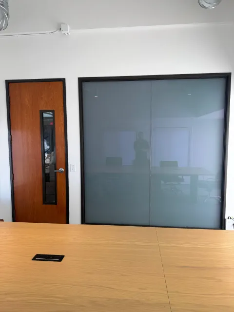 The same switchable glass wall seconds later in the frosted state, a flat even milky blue-white privacy panel on one switch