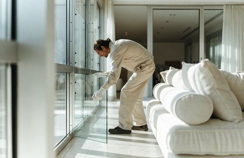 A glazier setting a large clear glass panel into a modern window frame in a bright living room — smart glass installs like any ordinary glass unit