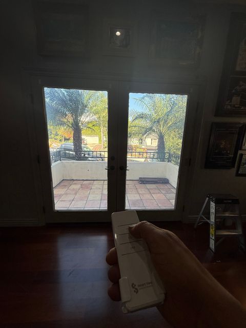 Switchable glass patio doors in a Los Angeles home in the clear state, the palm-lined patio visible, remote in hand