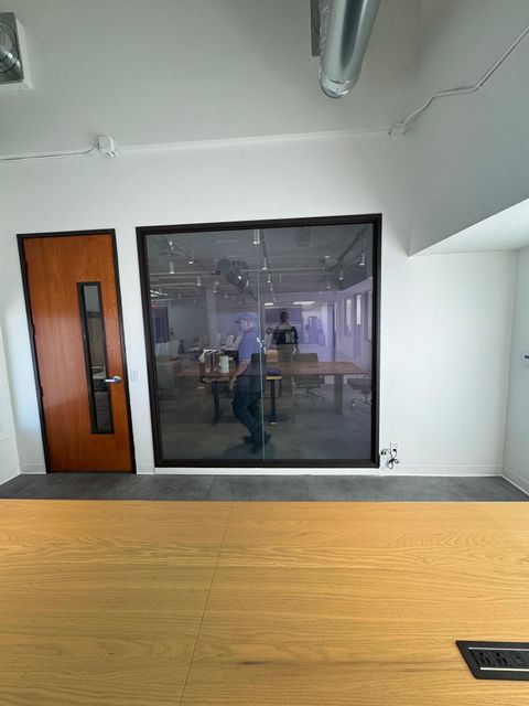 A Newport Beach office conference room behind a switchable glass partition in the clear state, the desks and room visible