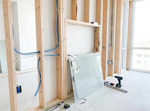 Wall under construction with wood stud framing and low-voltage wires run through the frame into the opening for a switchable smart glass panel