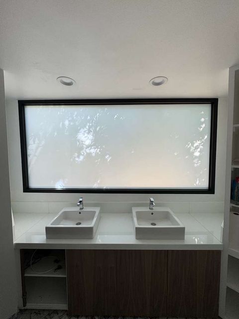 A frosted switchable privacy window above a double vanity in a Pasadena bathroom, the trees outside obscured for privacy
