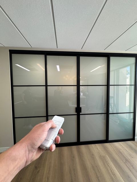 A steel-framed switchable smart glass partition in a Pasadena home, frosted to privacy with a remote in hand