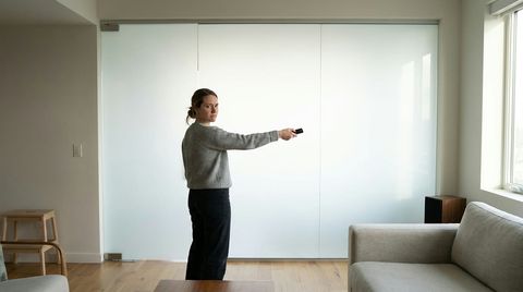 A woman pressing a remote at a large frosted smart glass wall that is stuck and won't switch to clear