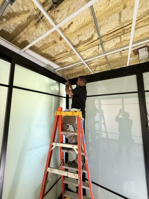 A Smart View installer on a ladder fitting a steel-framed switchable smart glass partition during a Santa Barbara install