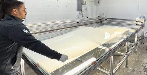 A technician cutting a custom panel of switchable smart film to size on an illuminated cutting table in the Canoga Park fabrication shop