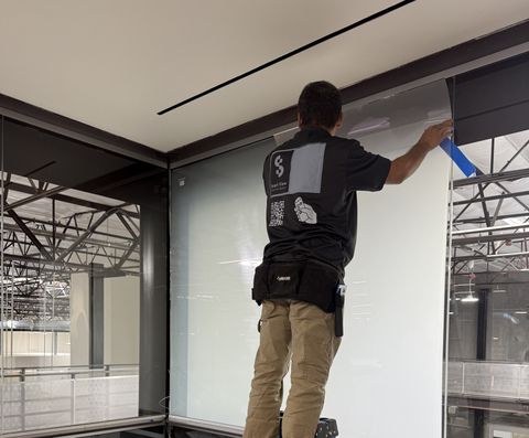 A Smart View technician on a ladder applying switchable smart film to a large existing glass wall