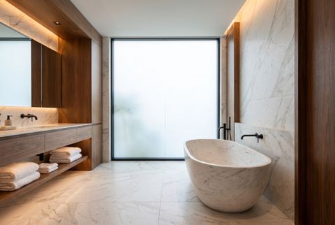A luxury bathroom window switched to frosted privacy with smart film, freestanding tub, soft daylight