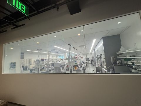 Smart film laboratory window in Los Angeles seen from the corridor, all four panels clear with the brightly lit lab benches and fume hoods beyond