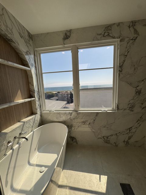 Smart glass bathroom in Hermosa Beach, casement window clear showing the ocean view over a marble freestanding tub