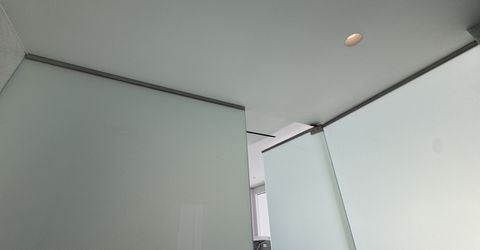 Ceiling detail of the Culver City shower partition, the frosted smart glass panels meeting the slim head rail with the door leaf standing open