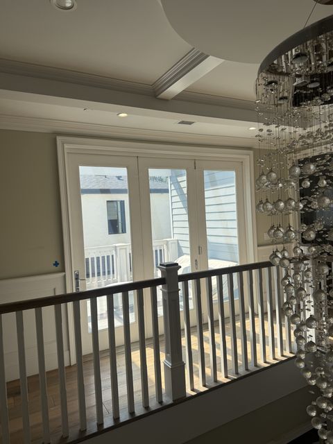 The Studio City smart glass bifold door switched clear, seen across the landing balustrade with the stairwell chandelier at right
