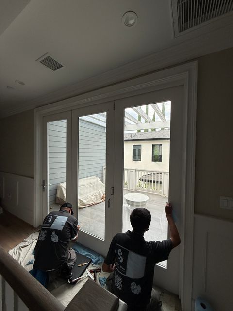 Two Smart View installers seen from behind, applying smart film to the Studio City smart glass bifold door from the second-floor landing