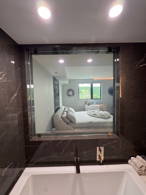 A West Hollywood marble bathroom with a switchable glass wall in the clear state, the bedroom visible through it